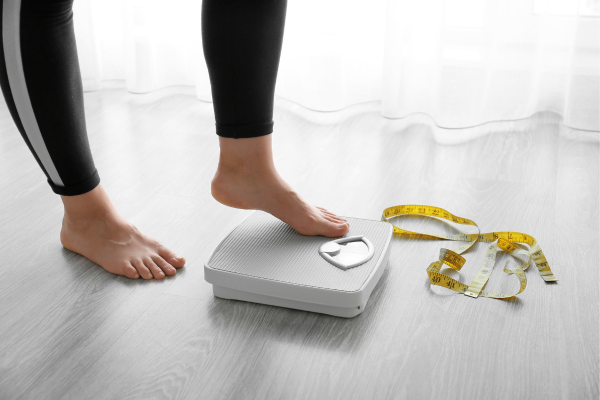 Person stepping on a scale with a measuring tape beside them, symbolizing weight loss goals.