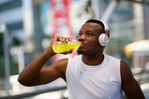 Athlete drinking an electrolyte drink for post workout hydration while wearing headphones outdoors.