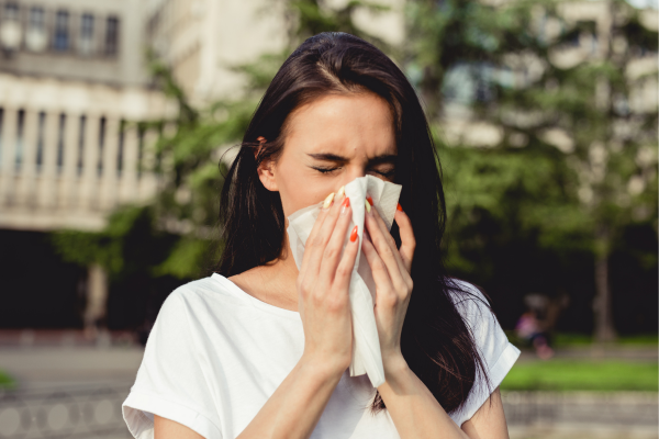 Woman experiencing allergy symptoms, using a tissue to alleviate nasal discomfort.