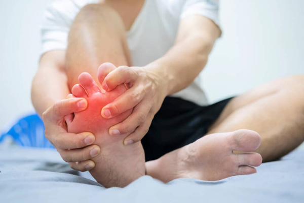 A person holding their inflamed big toe, a common area affected by gout flare-ups.